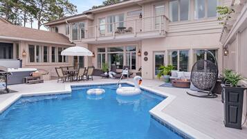 A swimming pool with two swan inflatable toys, a covered patio with outdoor furniture, and a large umbrella.
