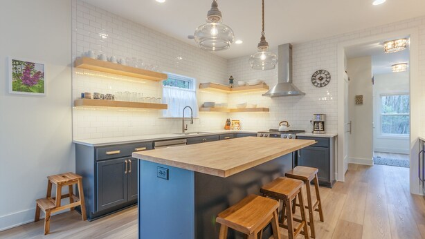 Una cocina moderna con una isla central, taburetes de madera e iluminación colgante.