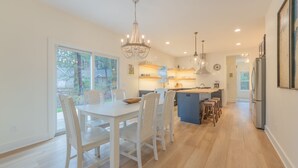 Una cocina moderna con armarios blancos, una isla central, iluminación colgante y vistas al exterior.