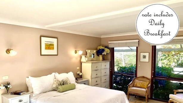A bedroom with a bed, nightstands, a dresser, and a chair. There is a window with a view of greenery outside.