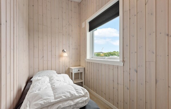 Un dormitorio con paredes de madera, una cama, una mesita de noche y una ventana con vistas a la vegetación.
