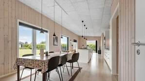 Eine moderne Küche mit Holzvertäfelung, ein Essbereich mit einem Tisch in Punkte-Muster und Blick ins Freie.