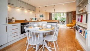A modern kitchen with white cabinets, a dining table with four chairs, and a bookshelf filled with books.