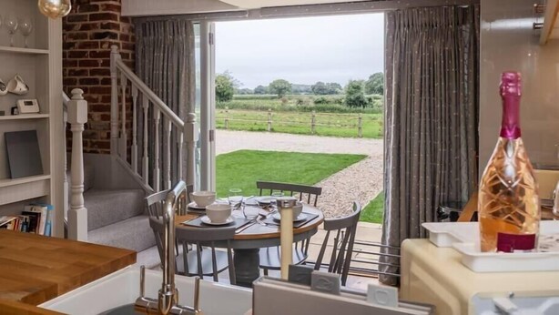 A dining area with a view of a grassy field through open doors.