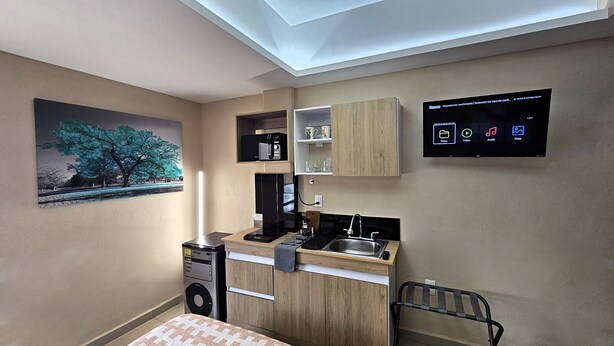 A compact kitchen with a built-in microwave, a coffee maker, and a sink. A flat-screen TV is mounted on the wall, displaying a menu interface.