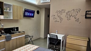 A modern hotel room with a bed, desk, and kitchenette.