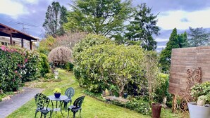 Un jardín con un banco de madera, una mesa con sillas y plantas en macetas.