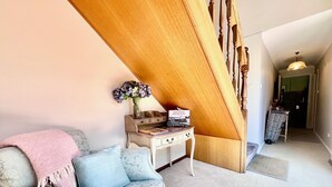 Una sala de estar acogedora con un sofá, una mesita con un jarrón de flores y una escalera que lleva a otra habitación.