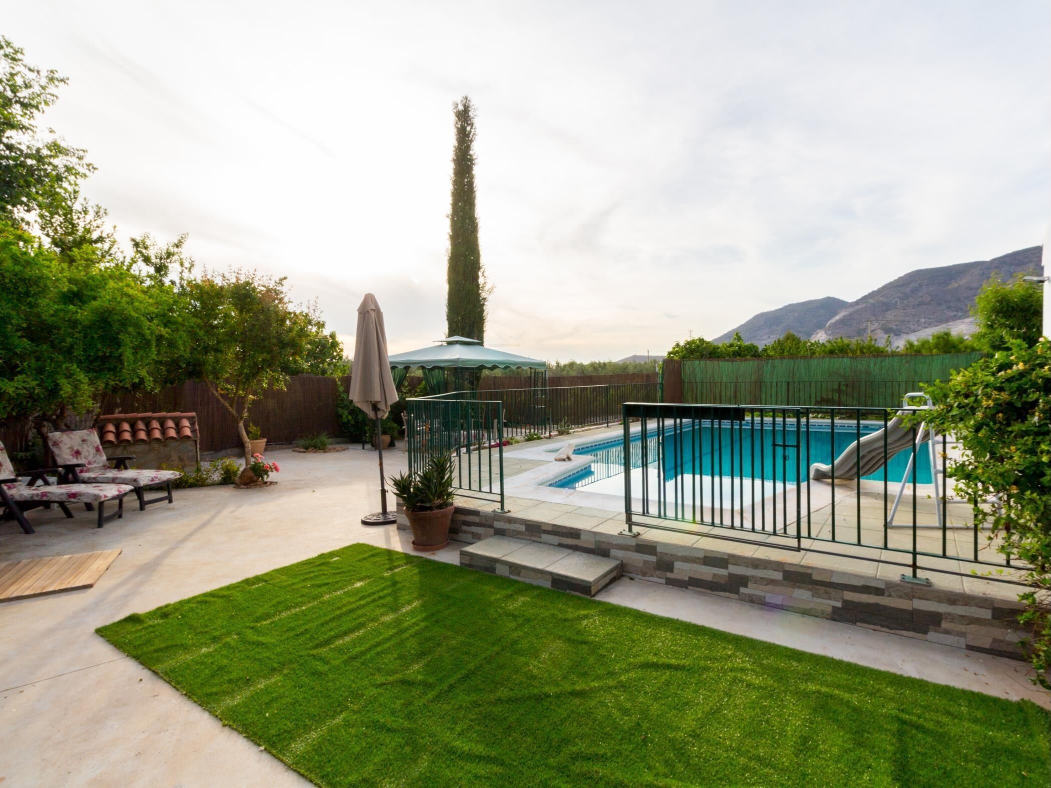 A backyard with a swimming pool, a lawn, and a patio area with outdoor furniture.