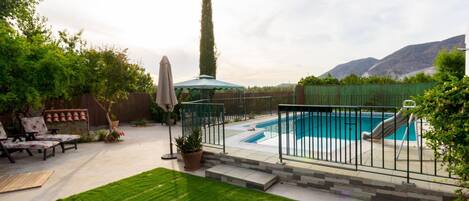 A backyard with a swimming pool, a lawn, and a patio area with outdoor furniture.