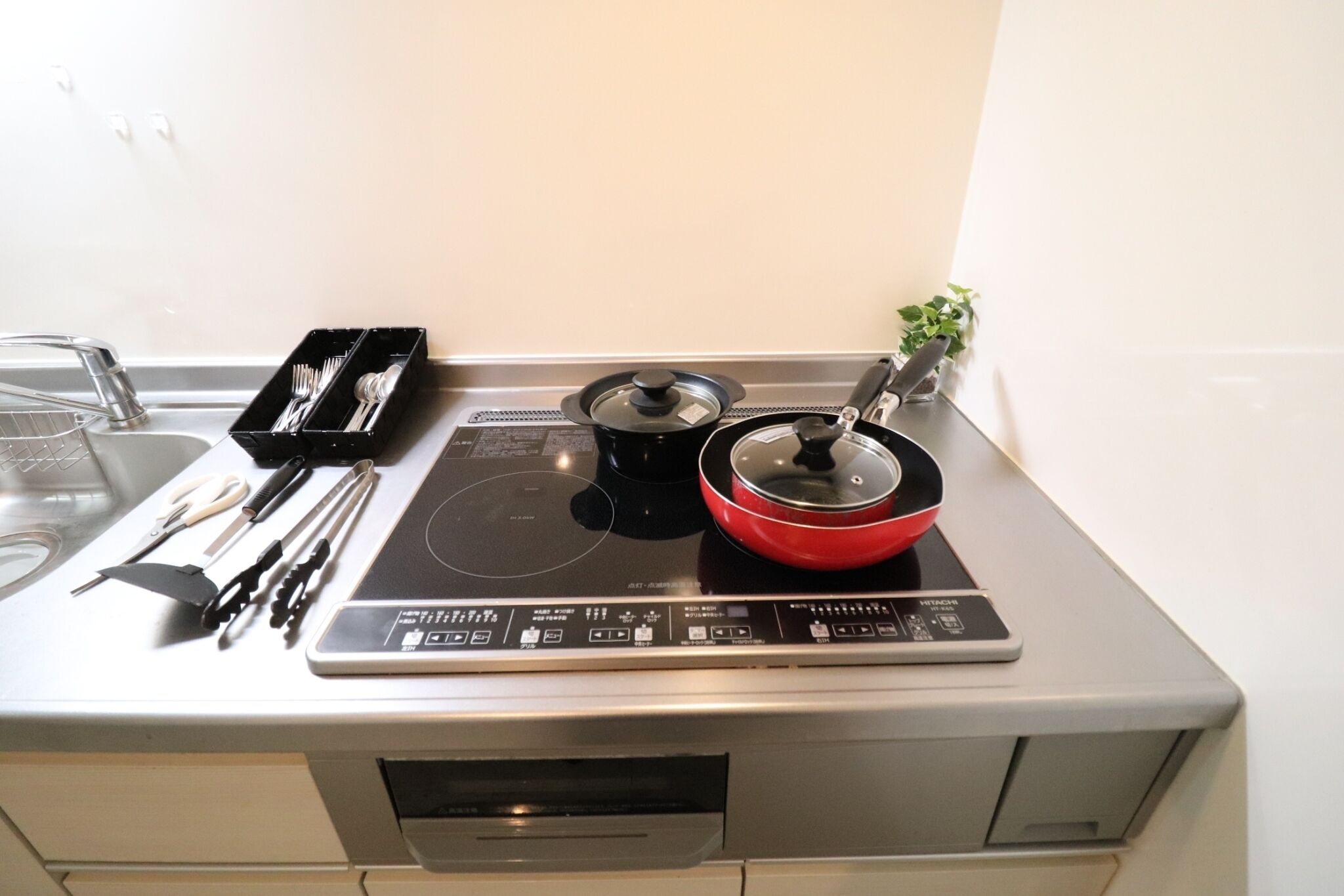 A kitchen with a built-in induction cooktop, a red pot, a black pot, and a utensil holder.