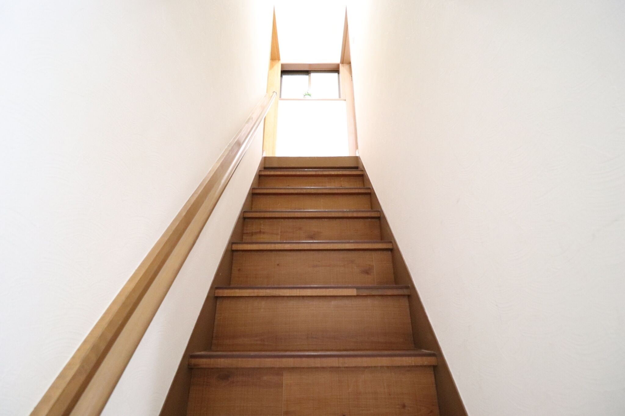 A wooden staircase with a handrail, leading to a window at the top.
