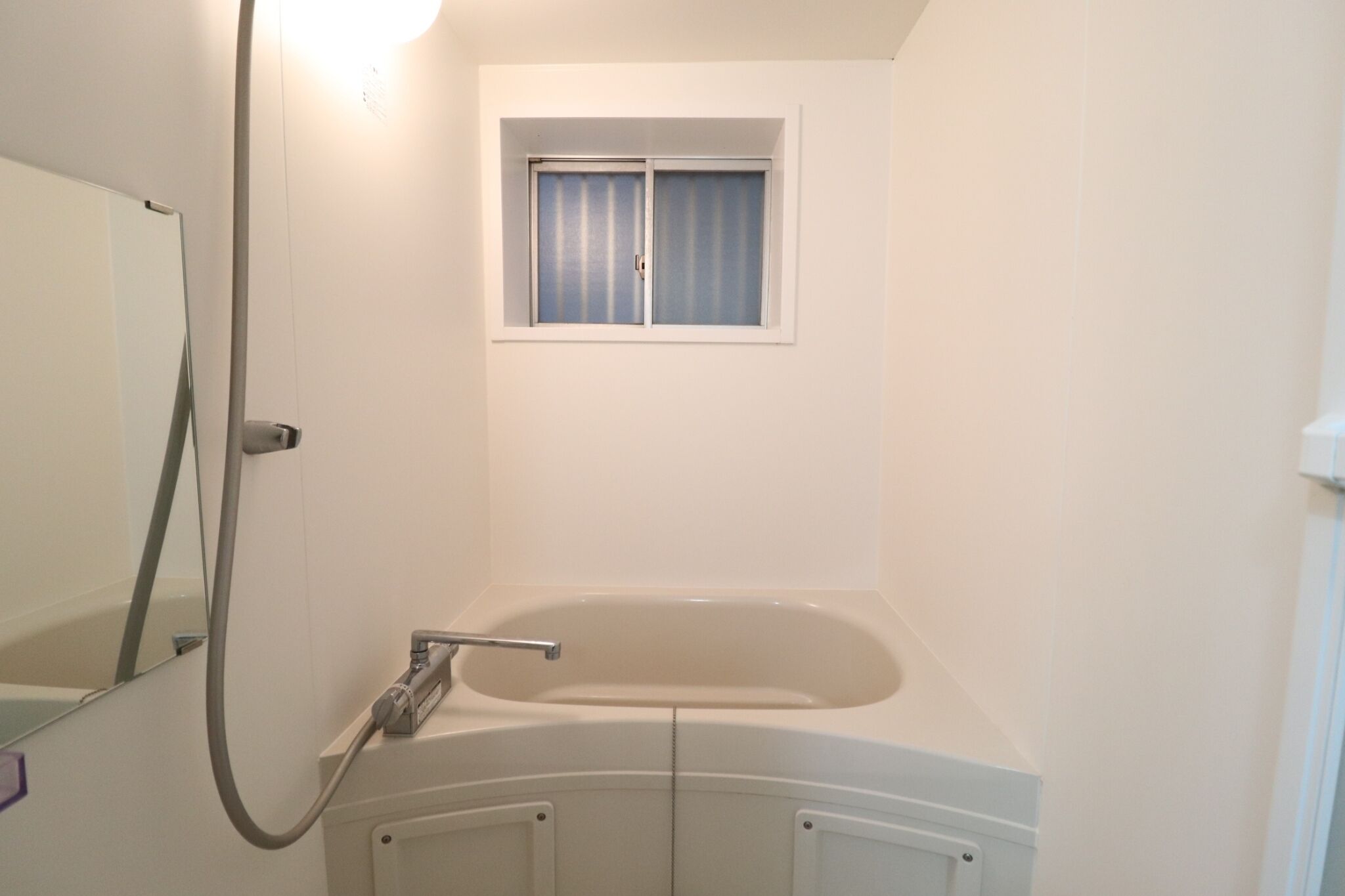 A bathroom with a bathtub, a window, and a shower.