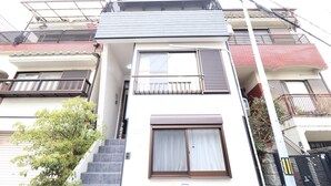 A multi-story residential building with a central staircase, a balcony with a metal railing, and a large window with a curtain. - Tsuruhashi East III (Osaka)