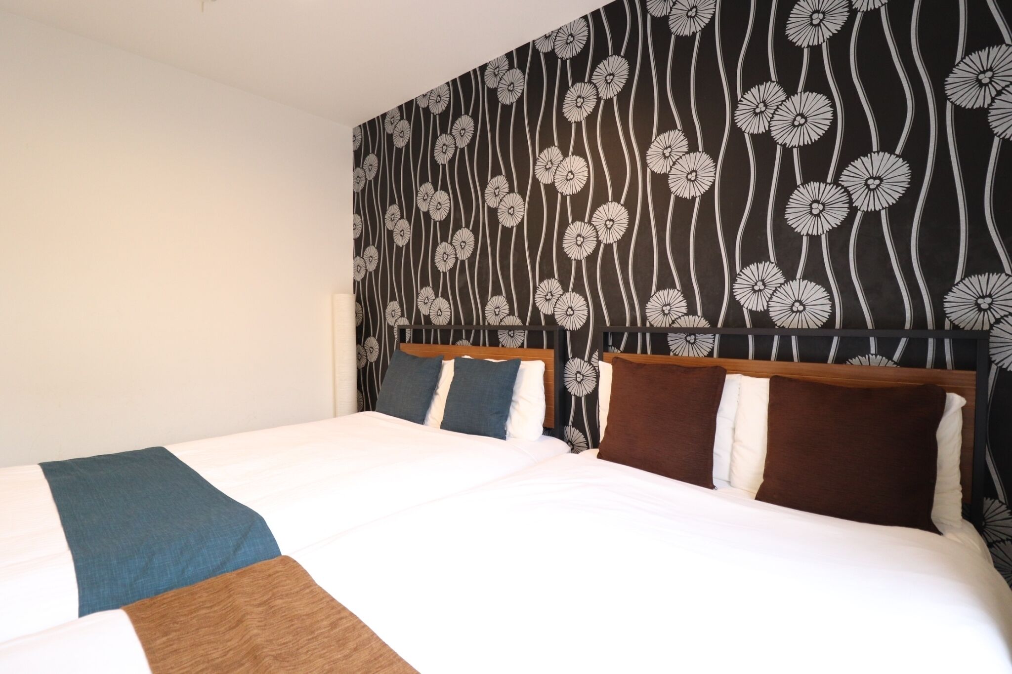 A double bed with a wooden headboard, white bedding, and a floral-patterned wallpaper.