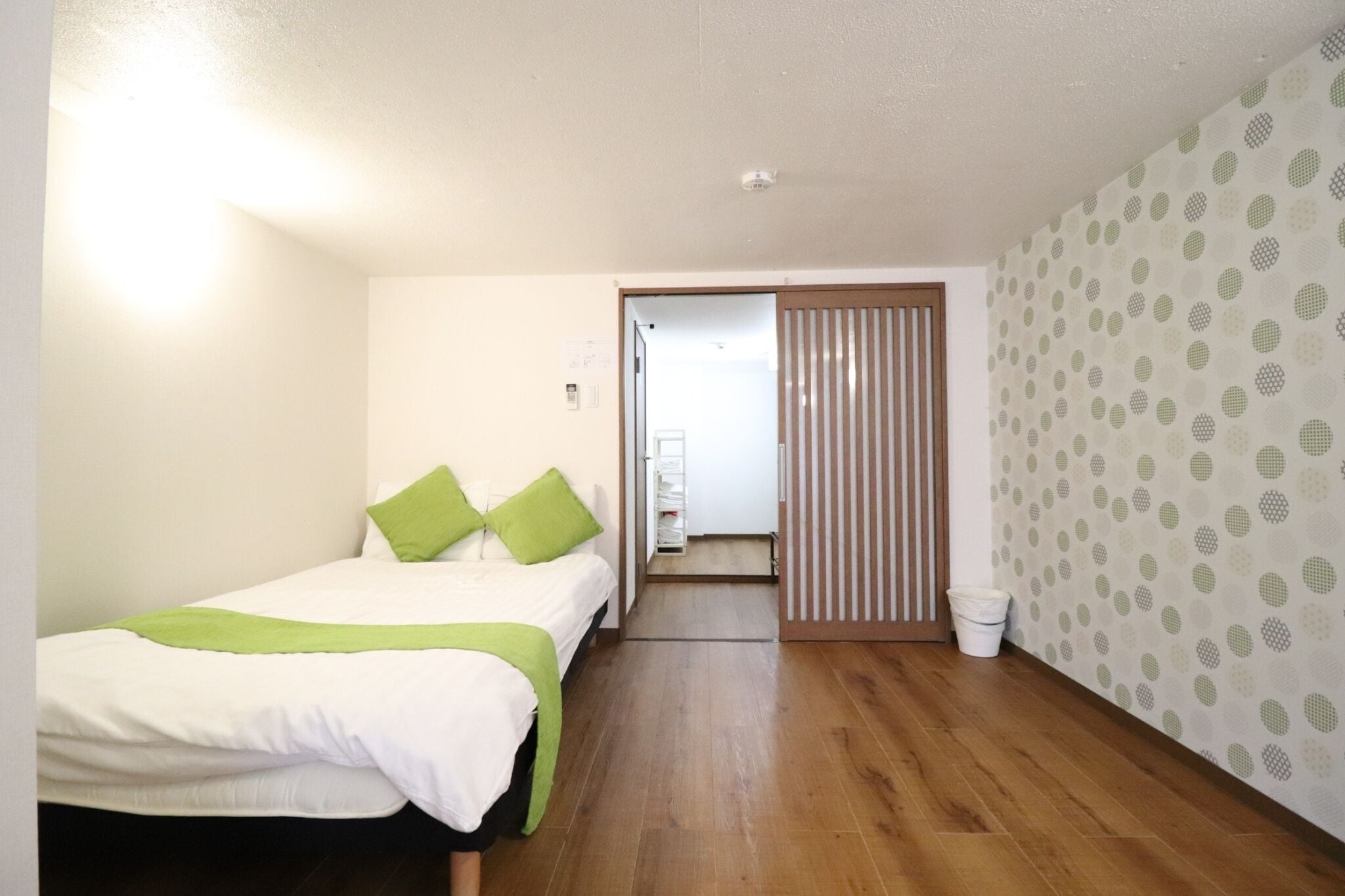 Un dormitorio con cama, suelo de madera, una puerta que da a otra habitación y pared con diseño.