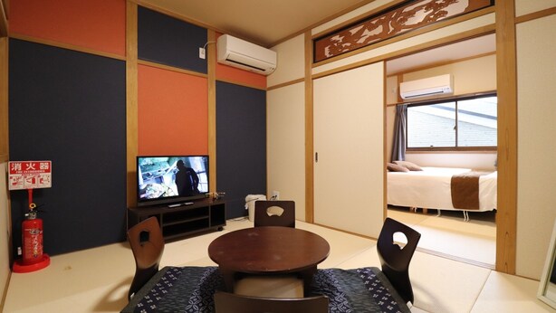 A traditional Japanese room with tatami flooring, a tatami mat table, a television, a bed with a futon, and a sliding door. - Tsuruhashi East III (Osaka)
