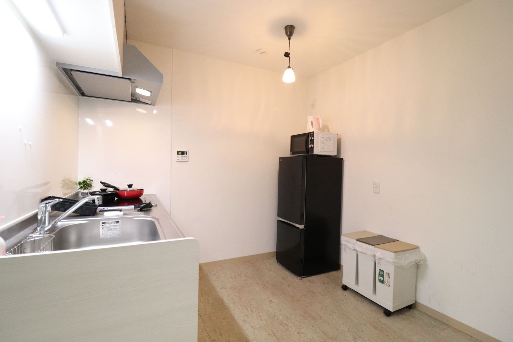 A compact kitchen with a sink, a black refrigerator, and a small trash bin.