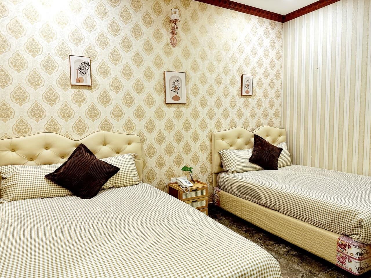 A hotel room with two beds, each with a tufted headboard and checkered bedding. There are wall-mounted light fixtures and framed pictures on the walls.