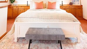 Un dormitorio con techo inclinado, una cama con reposabajares, armarios de madera y un ventanal grande.