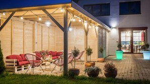 A covered outdoor seating area with a wooden bench and chairs, string lights, and potted plants. - Beach front home in Nowecin with sauna (Nowecin)