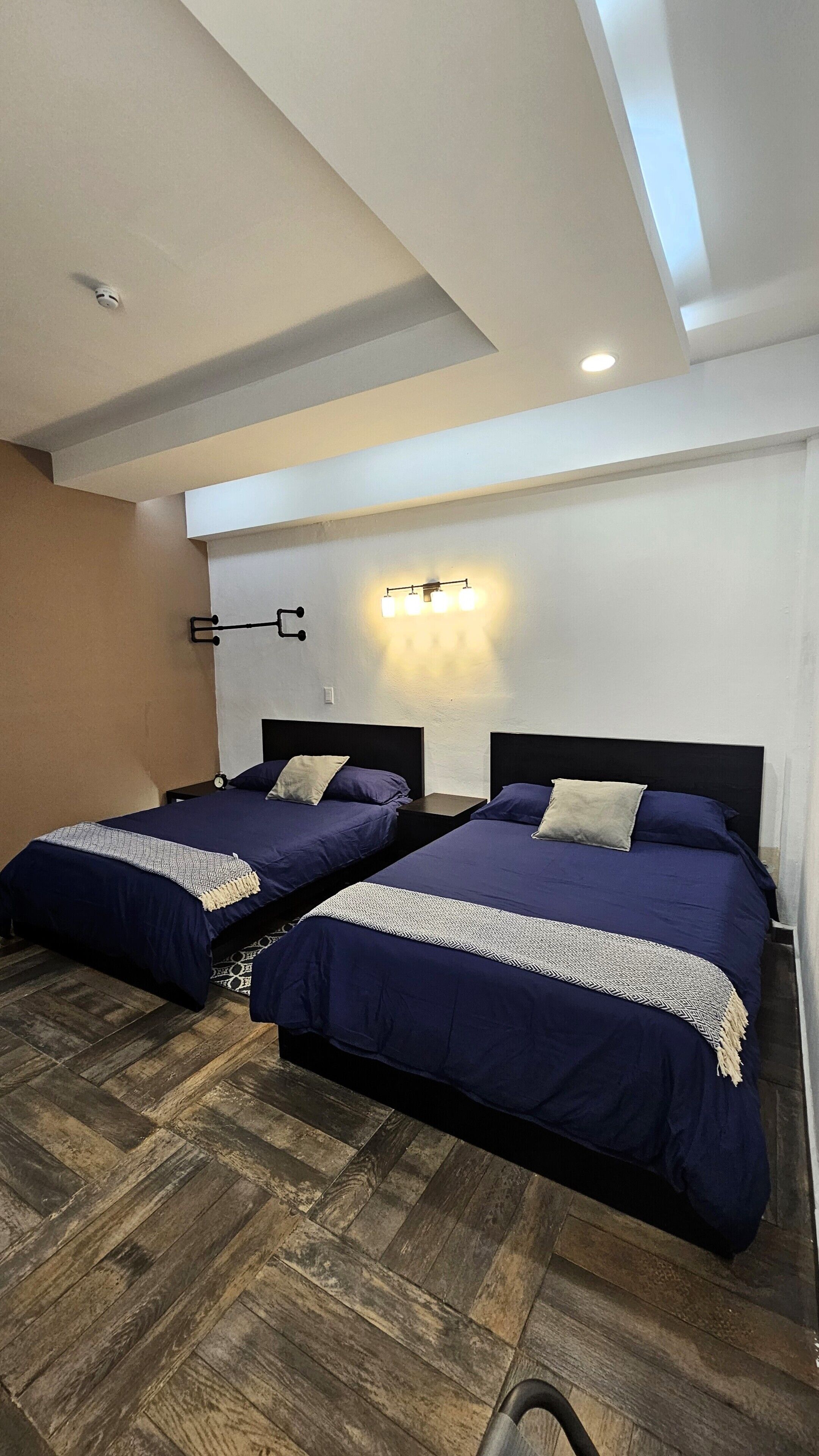 Een hotelkamer met twee bedden, houten vloeren, een witte muur en een plafondlamp.