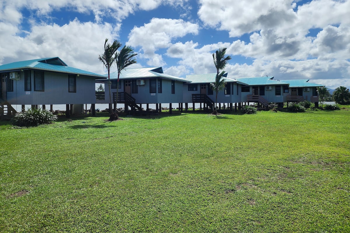 A row of two-story buildings with a blue roof, a grassy lawn, and a clear sky.