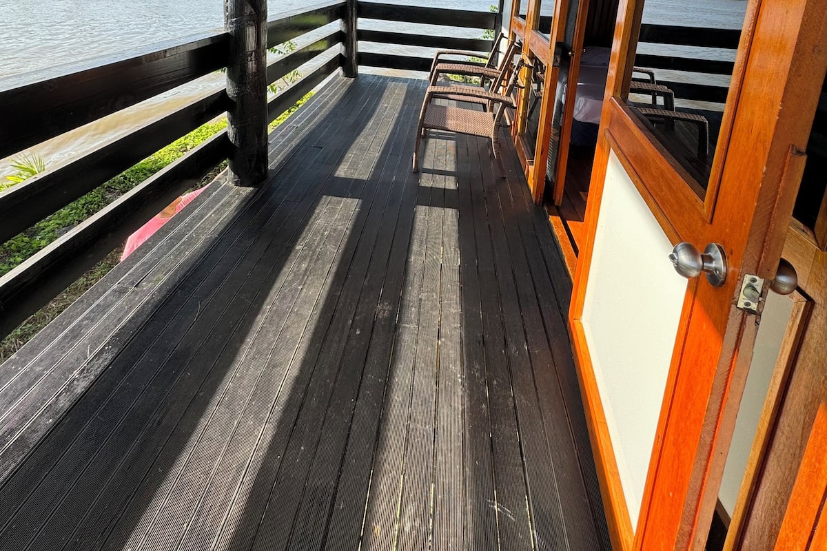 A wooden deck with a railing overlooking a body of water, featuring a bench and a door.