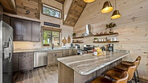 Una cocina moderna con paredes de madera, una isla central con taburetes de bar, electrodomésticos de acero inoxidable y una lámpara colgante.
