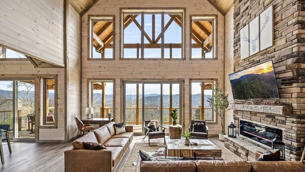 Un salón amplio con chimenea grande, vigas de madera y vistas panorámicas a la montaña.