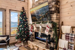 A cozy room with a fireplace, a Christmas tree, and a scenic view through the window. - Mountain Views, Barrel Sauna, Hot Tub, 3 King Suites, Game Room, Pool (Sevierville)