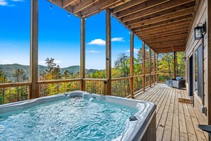 Una terraza de madera con un jacuzzi, con vista a un paisaje montañoso.