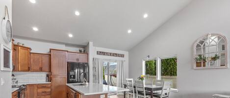 A kitchen with wooden cabinets, a stainless steel refrigerator, and a dining area with a table and chairs.