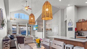 A spacious living area with a high ceiling, a dining table with chairs, a sofa, and a TV mounted on the wall. - Spacious Modern Home—Fire Pit, Basketball Hoop, Pop-A-Shot & Kids' Toys for Family Fun! (Coeur D Alene)