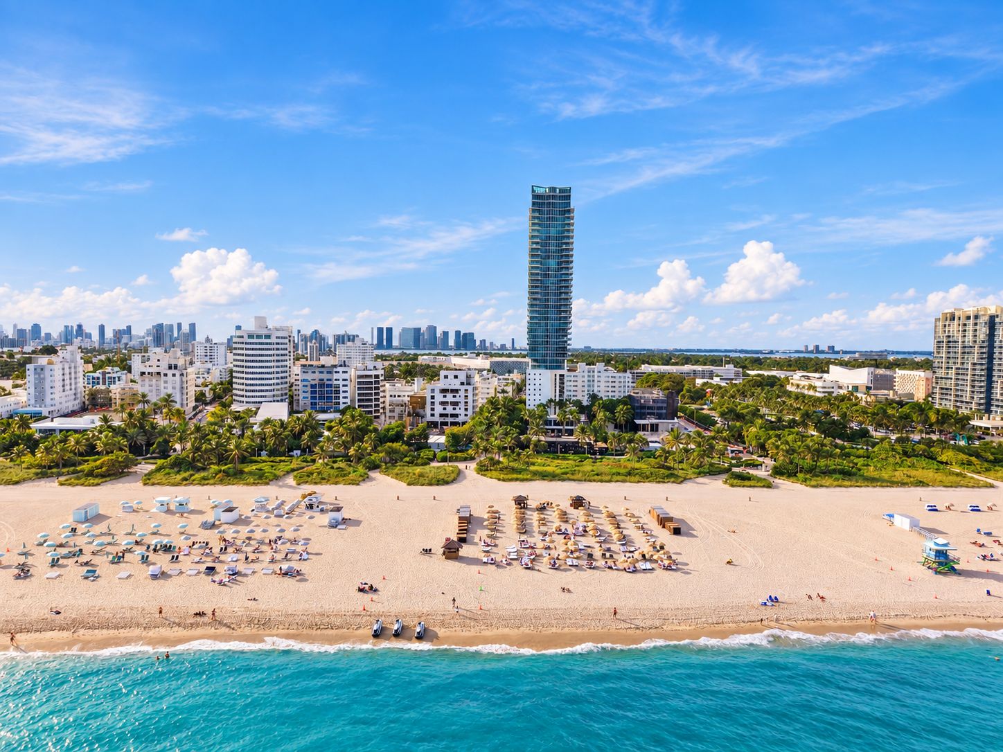 A beach with sun loungers and umbrellas, a tall building in the background, and a city skyline.