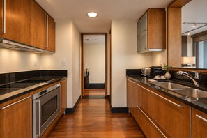 A modern kitchen with wooden cabinets, a black countertop, stainless steel appliances, and a view into the dining area.