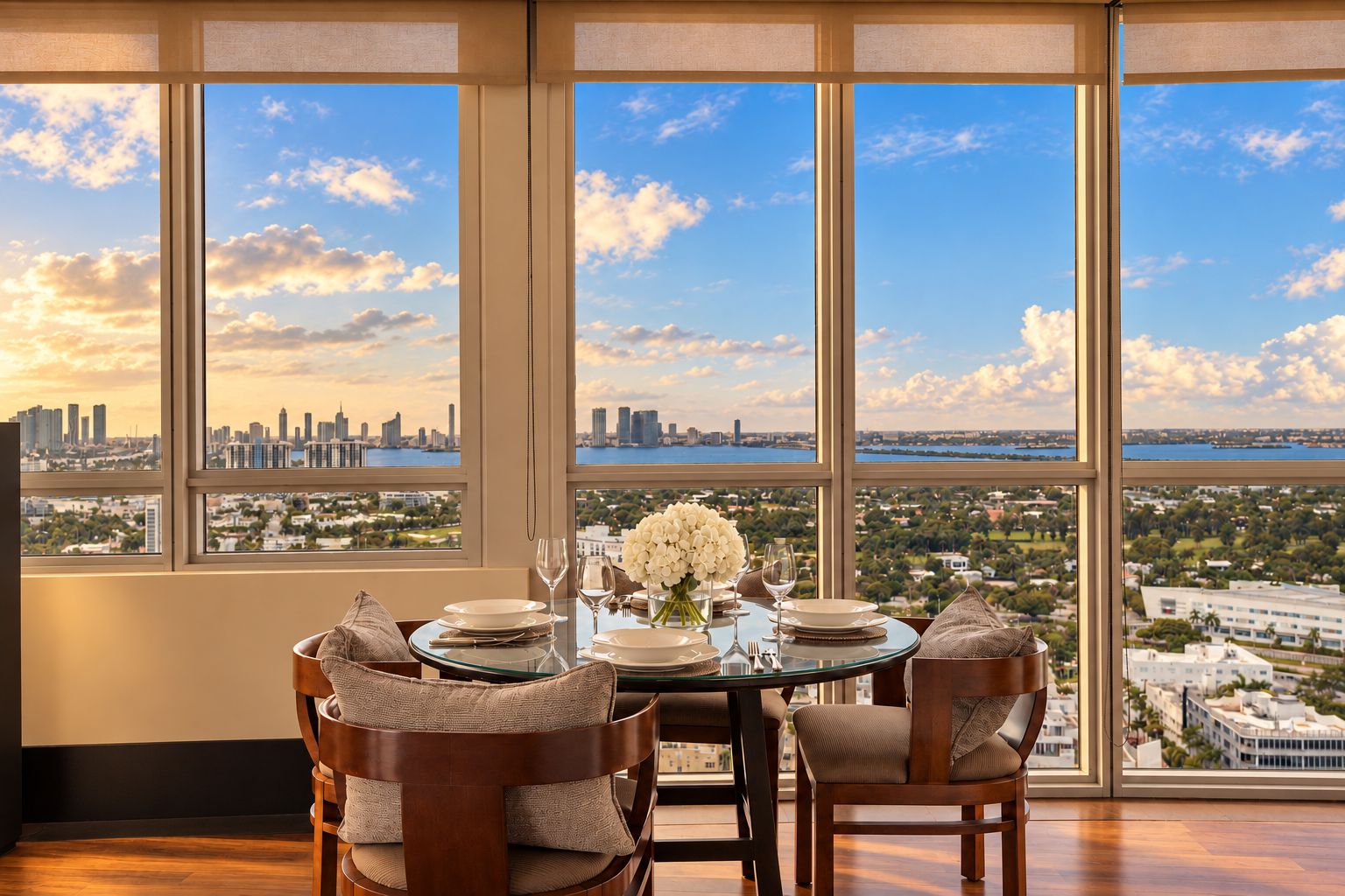 Comedor con una mesa dispuesta para cuatro personas, y ventanas amplias que ofrecen vista panorámica de la ciudad.