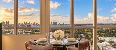 Comedor con una mesa dispuesta para cuatro personas, y ventanas amplias que ofrecen vista panorámica de la ciudad.