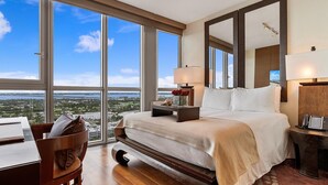 Ett rymligt hotellrum med en stor säng, ett skrivbord och utsikt över stadsbilden genom stora fönster.