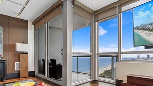 Ett modernt hotellrum med stora fönster som erbjuder utsikt över en strand och stadens silhuett.