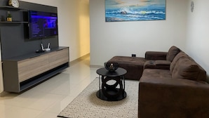A modern living room with a flat-screen TV, a brown sofa, a patterned rug, and a painting of a seascape. - A Two-bedroom Holiday Apartment, at the Heart of South Beach Durban (Durban)