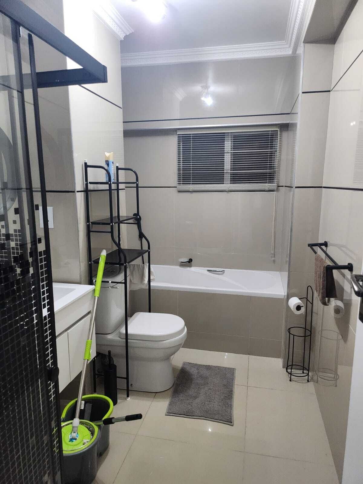 A small bathroom with a toilet, a bathtub, a window, a mop, and a broom.