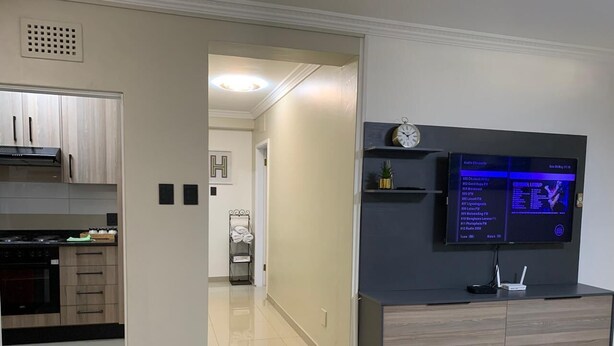 A modern kitchen with a built-in oven, a dining area with a table, and a living room with a flat-screen TV. - A Two-bedroom Holiday Apartment, at the Heart of South Beach Durban (Durban)