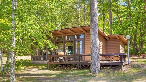 Une cabane en bois dotée de grandes fenêtres, d’une terrasse et d’un barbecue.