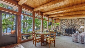 Un intérieur en bois avec une cheminée en pierre, de grandes fenêtres et une table ronde entourée de chaises.