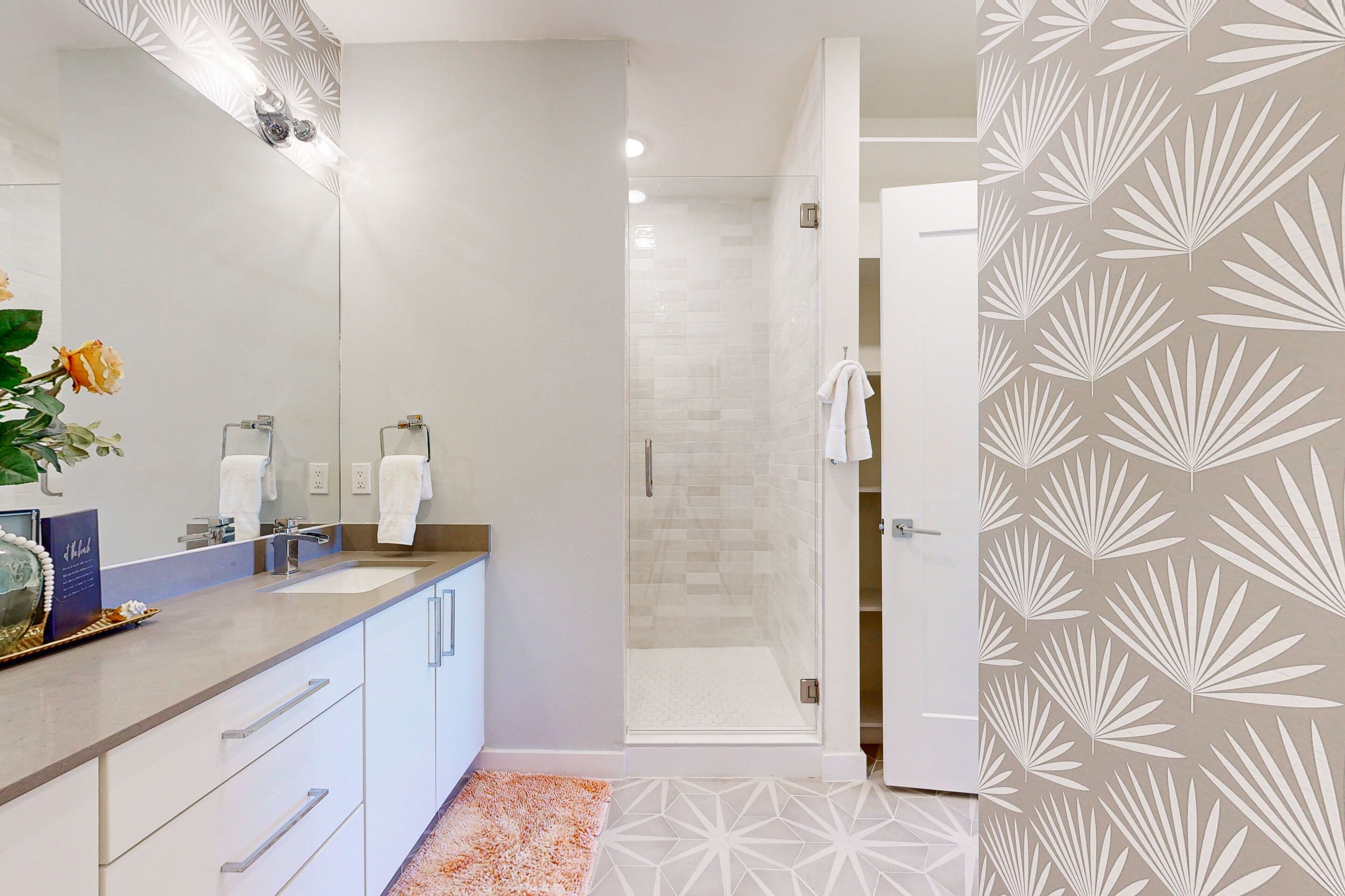 A modern bathroom with a glass shower enclosure, a vanity with a mirror, and a patterned wall.