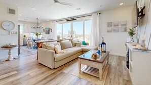 A spacious living area with a beige sofa, a coffee table, and a dining area with a chandelier. - Resort Style Pools, Boardwalk to the Beach (Port Aransas)