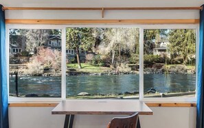 A room with a large window overlooking a river, a wooden desk, and a chair.