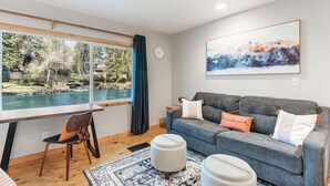 Un salon moderne avec une grande fenêtre, un canapé gris, un bureau en bois et un tapis.