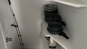 Uma cozinha pequena com prateleiras brancas, um esfregão, um aspirador de pó e uma cafeteira.
